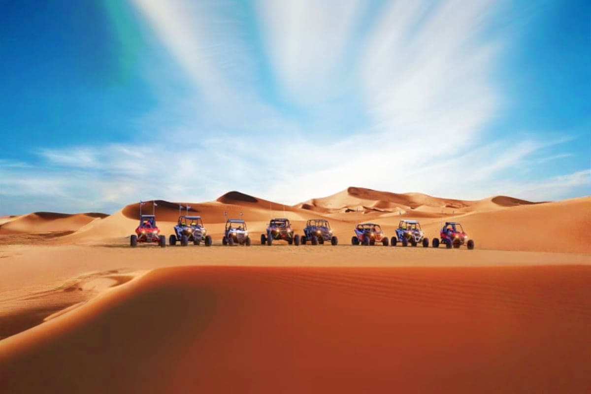 Group of tourists posing with yellow and black dune buggies on orange sand dunes under blue sky in Dubai desert (5)