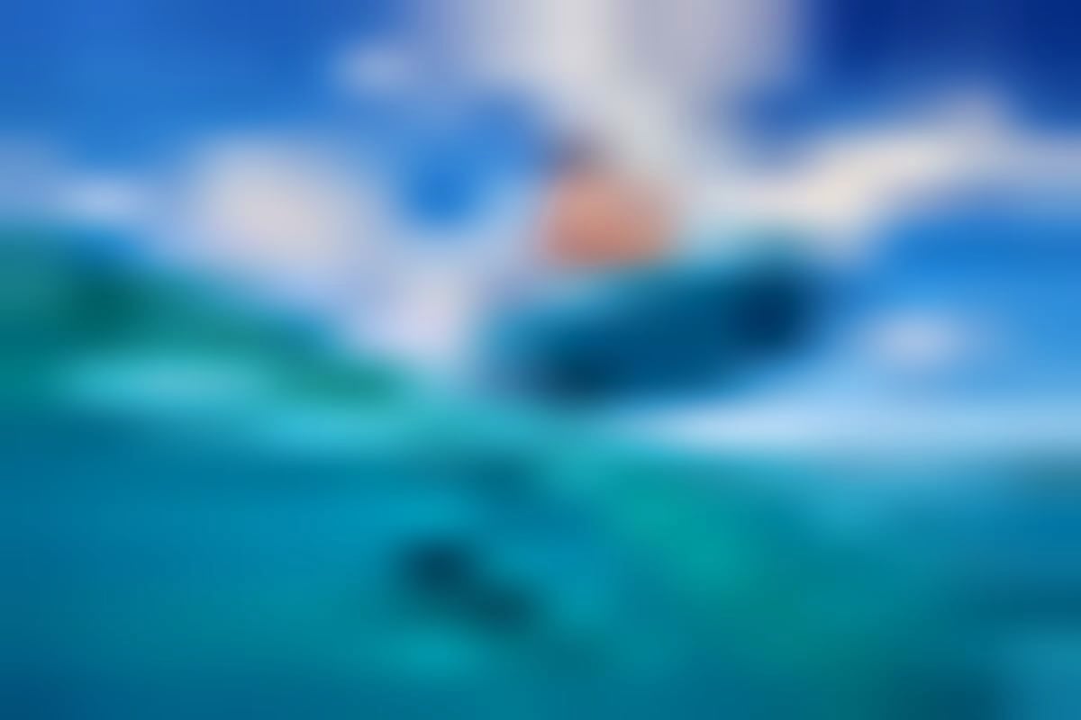 Aerial view of an e-foil rider gliding across turquoise Arabian Gulf waters under a blue sky with white clouds