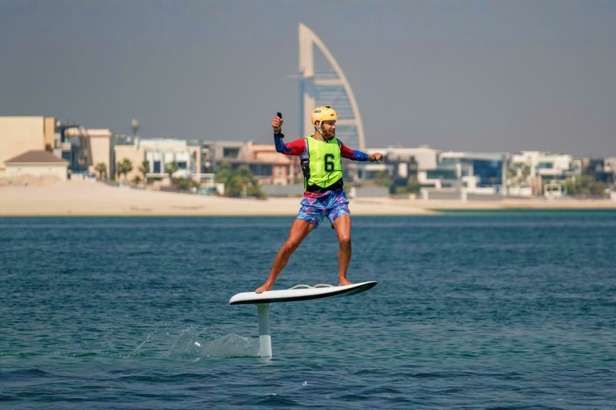 Foil boarder in neon vest riding electric hydrofoil board on Dubai waters with Burj Al Arab sail-shaped hotel in background