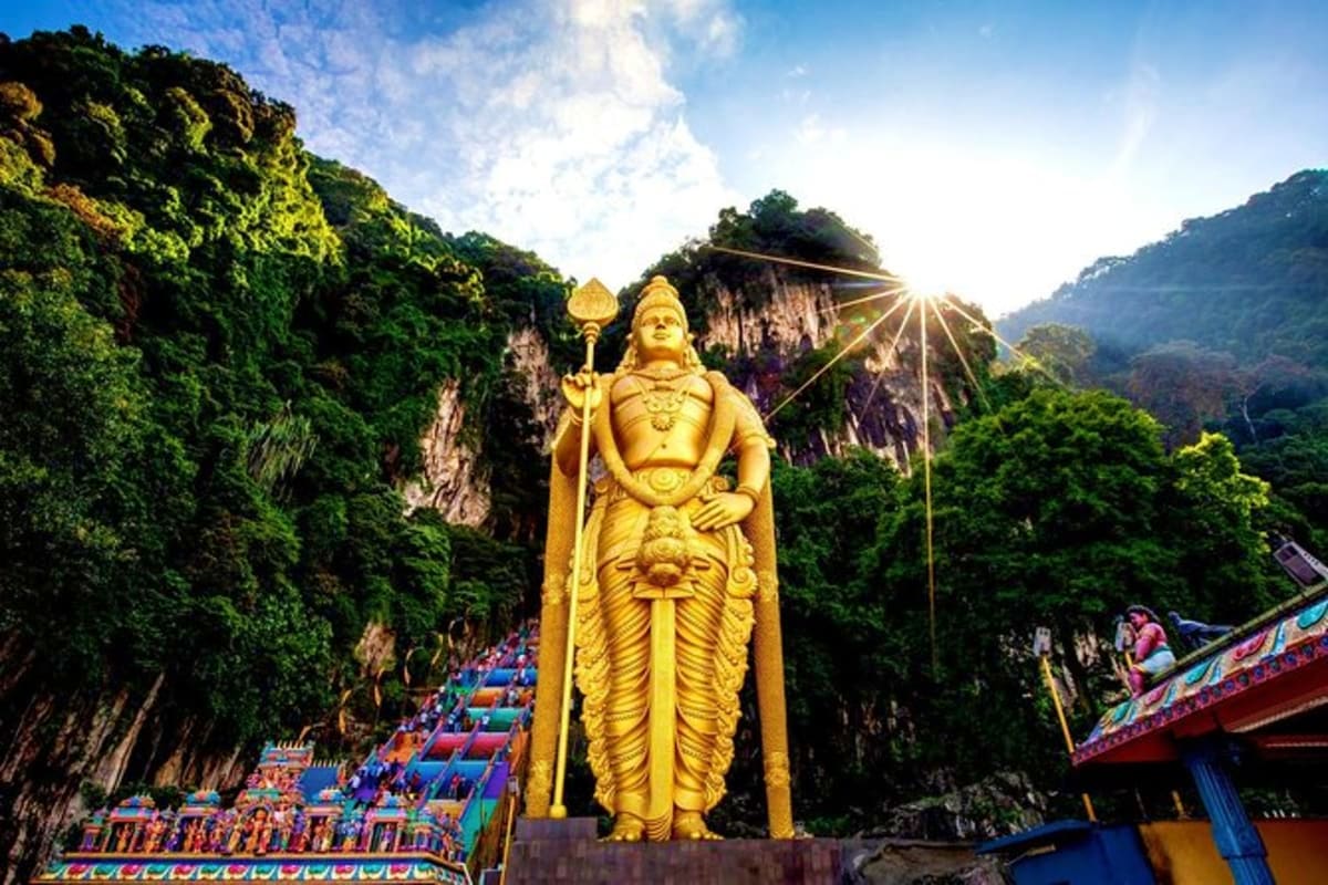 Grand Kuala Lumpur with Putrajaya and Batu Caves Private Tour Golden statue of Lord Murugan at Batu Caves entrance with colorful steps and limestone cliffs in background