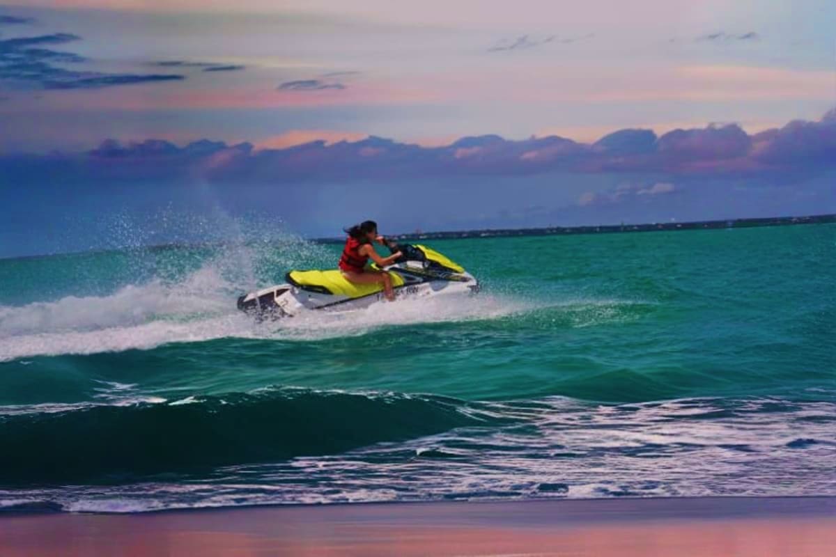 Person riding yellow jet ski on turquoise ocean waves at sunset in Dubai