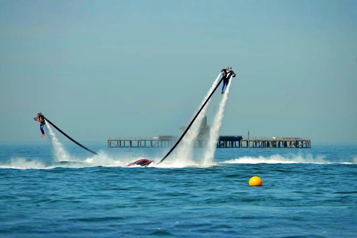 Person flying on jetpack over water at sunset with mountains and industrial structures in background (5)