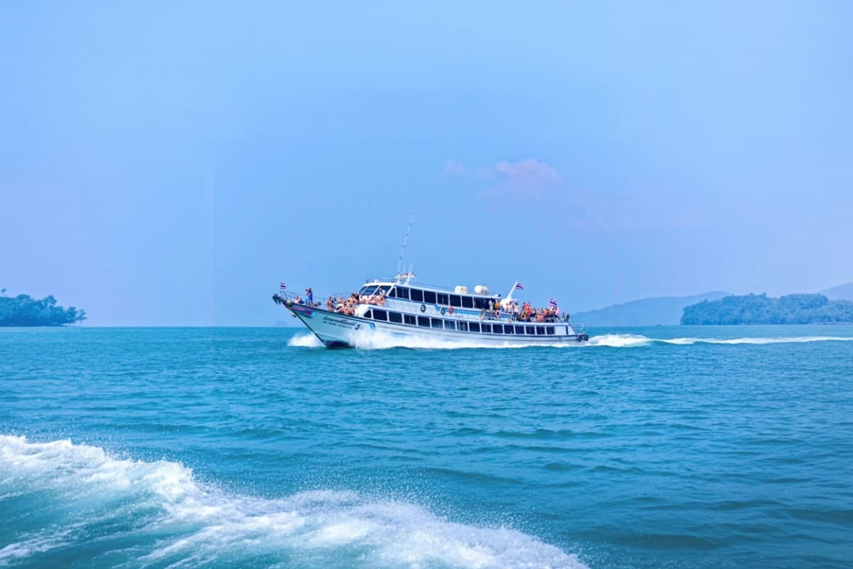 White and blue passenger ferry boat carrying tourists on turquoise ocean waters with tropical islands in background