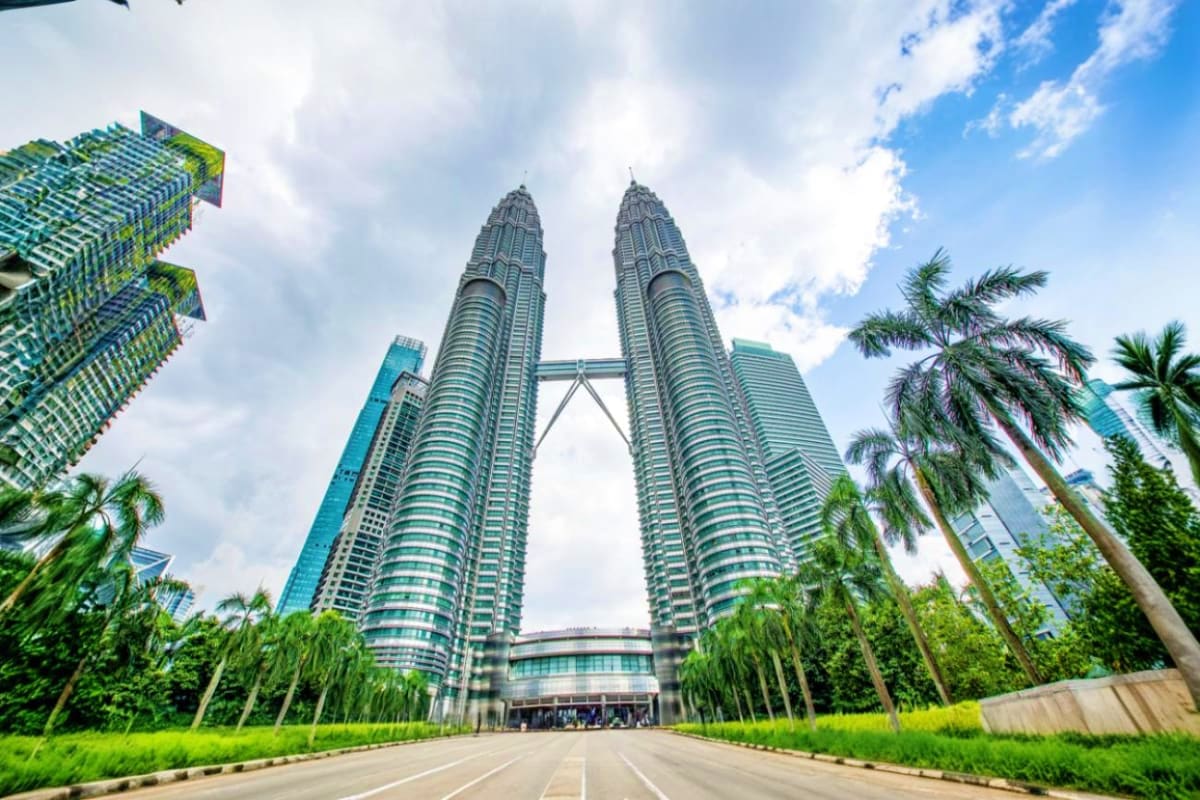 Petronas Twin Towers in Kuala Lumpur with palm trees lining the street and blue sky with clouds