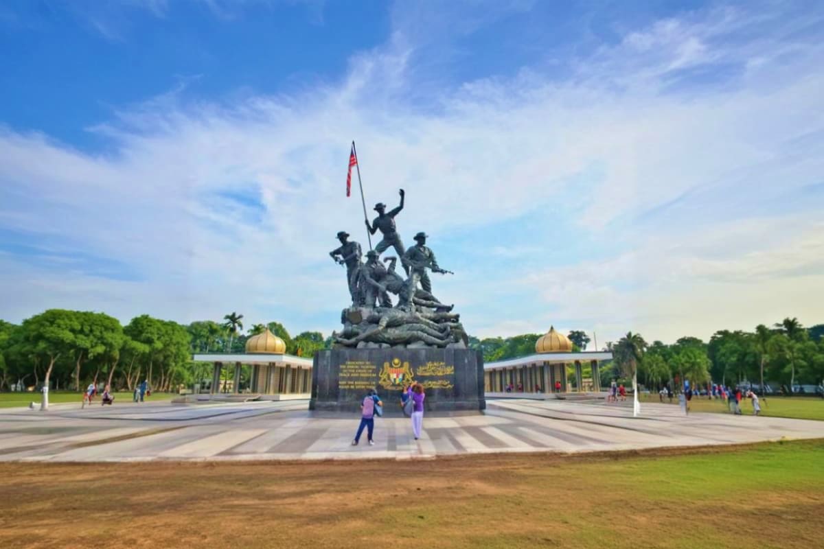 Monument of soldiers holding Malaysian flag at Merdeka Square in Kuala Lumpur with palm trees and golden domes in background