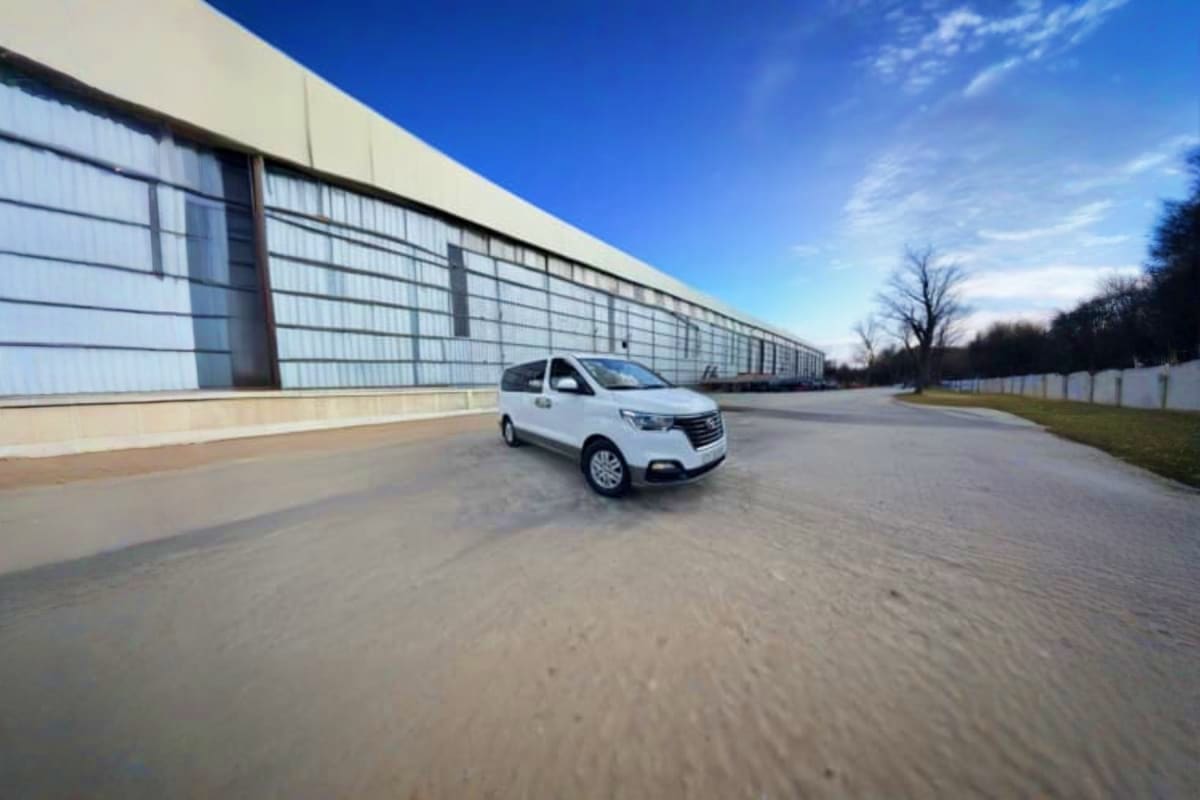 White minivan parked on empty asphalt lot in front of large modern warehouse building with clear blue sky