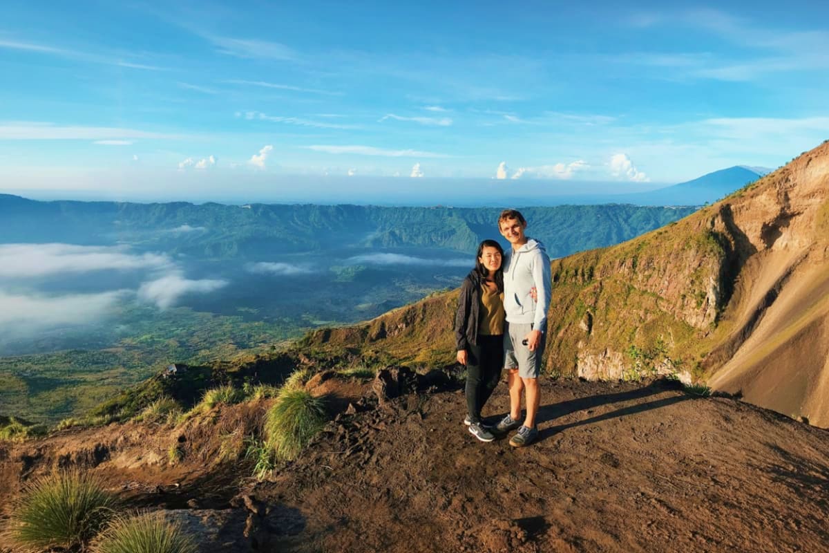 Two hikers standing on Mount Batur's volcanic ridge overlooking misty valleys and distant mountains at dawn