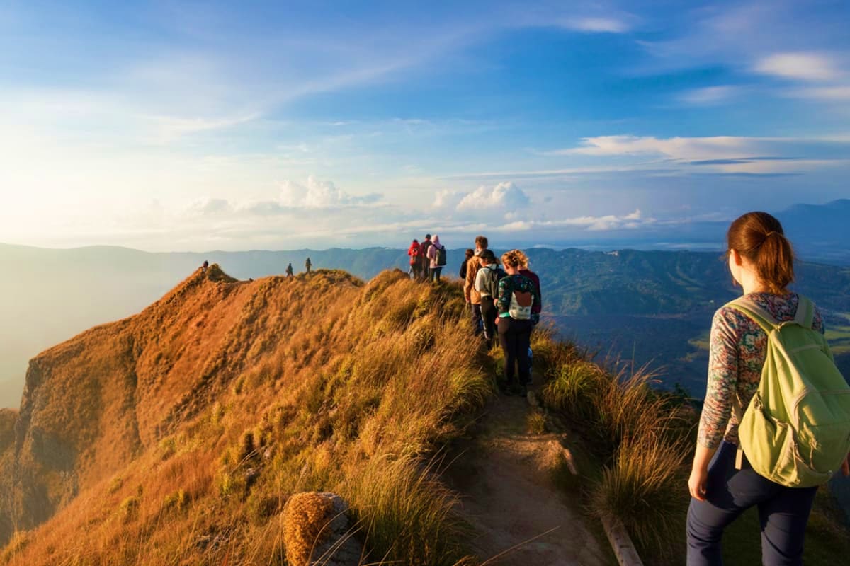 Group of hikers trekking along a scenic mountain ridge at sunrise with expansive valley views below