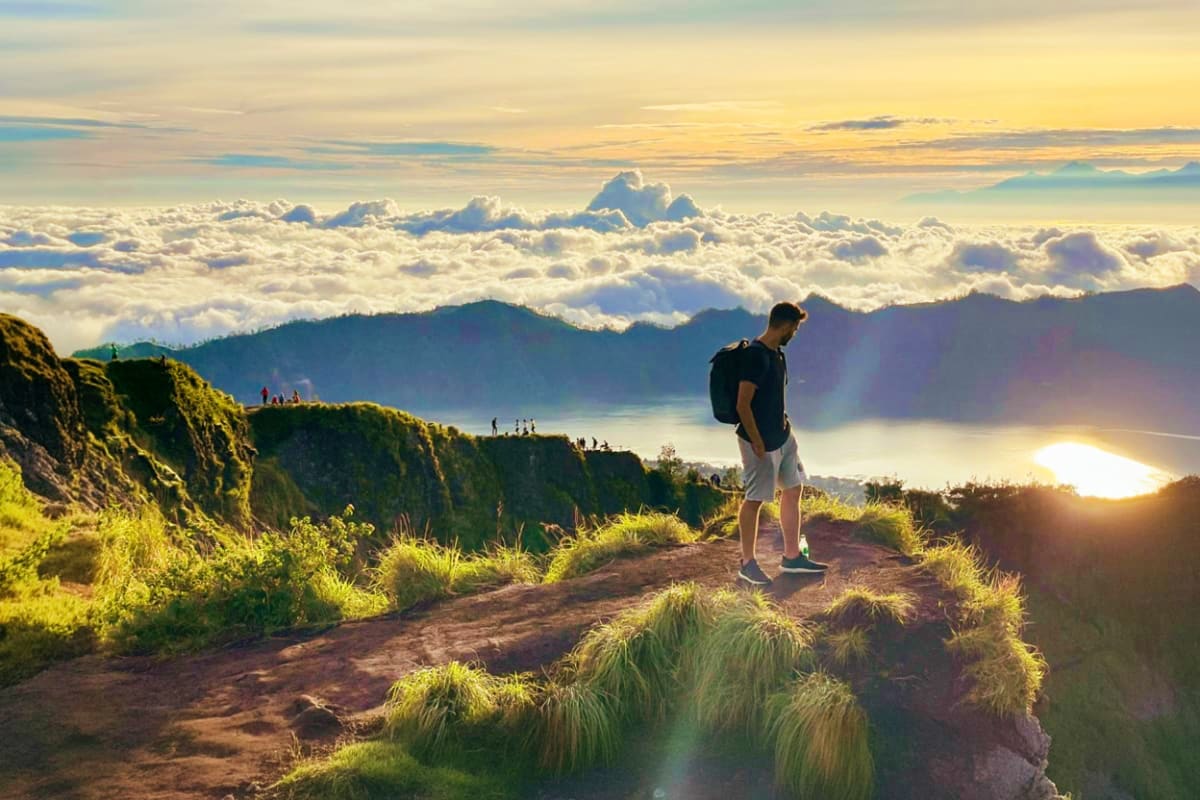 Hiker standing on mountain ridge at sunrise overlooking clouds and volcanic landscape during Mount Batur trek