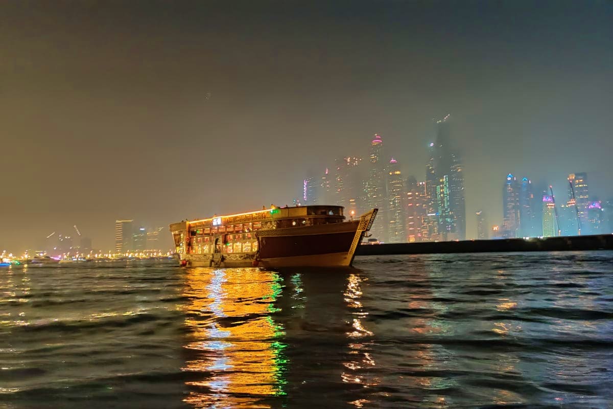 Luxury white yacht anchored at night with illuminated Dubai Marina skyscrapers and blue-lit waterfront buildings in background (5)