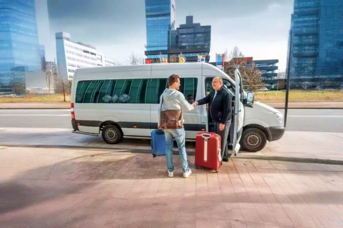 Passenger boarding white van with luggage at urban transfer pickup location with modern buildings in background