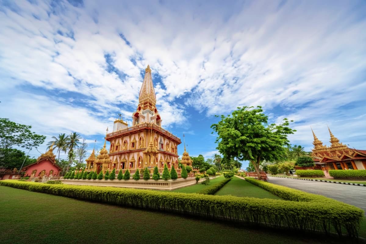 Buddhist temple with red and gold architecture, manicured gardens, and ornate spires in Phuket, Thailand