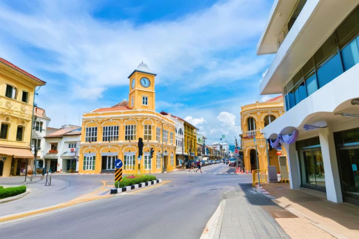 Historic yellow building with clock tower on tree-lined street in Phuket Old Town during daytime