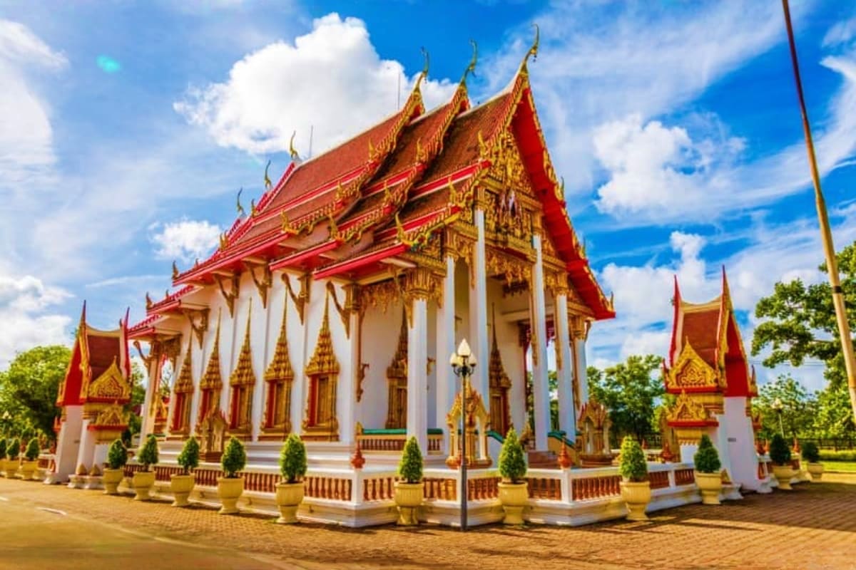 Traditional Thai Buddhist temple with red and gold roofs, white columns, and ornate decorative spires under blue sky