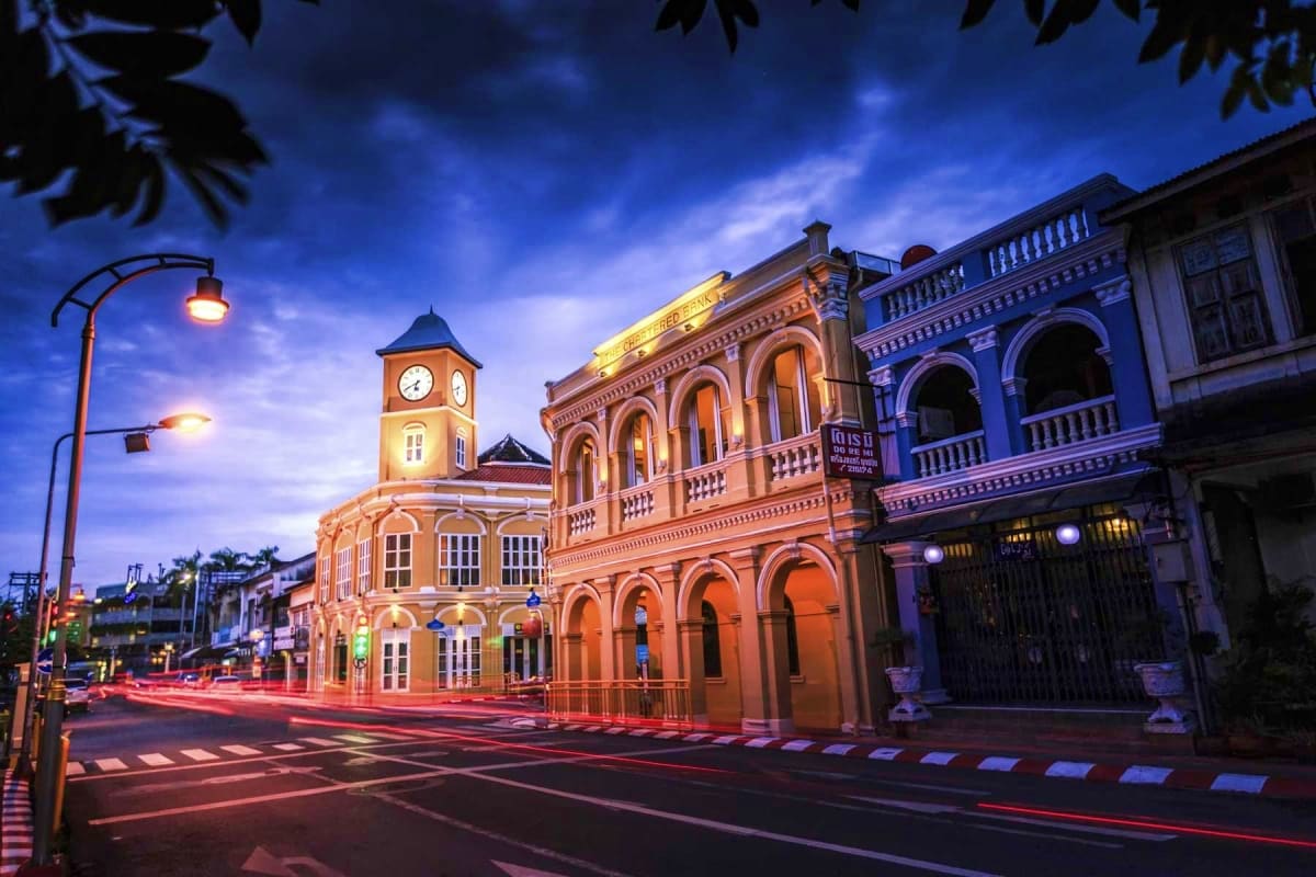 Historic colonial architecture with illuminated clock tower and buildings at dusk in Phuket Old Town, Thailand