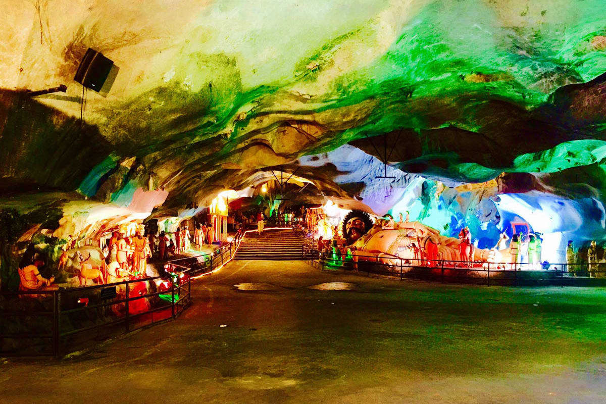 Colorful illuminated cave interior with painted Buddhist statues and figures along pathway in Ramayana Cave attraction