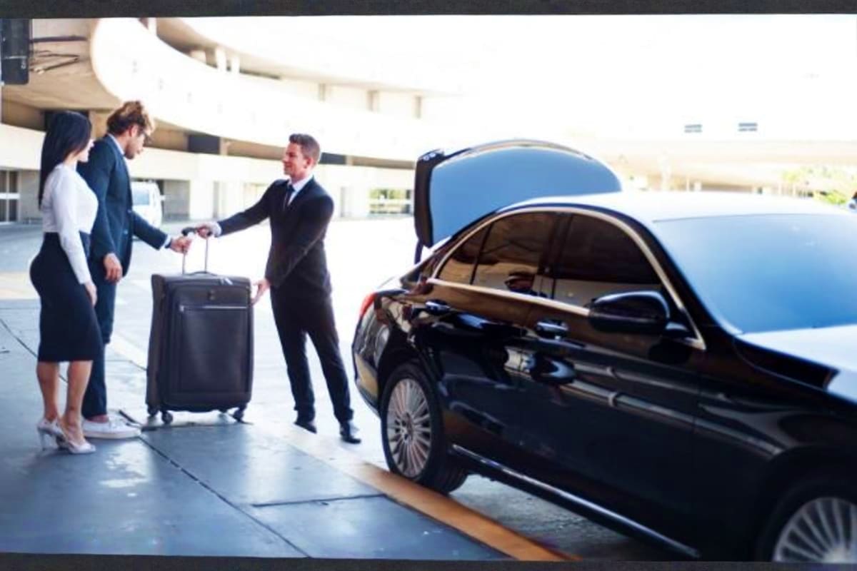 Business professionals with luggage greeting driver next to black luxury car at airport