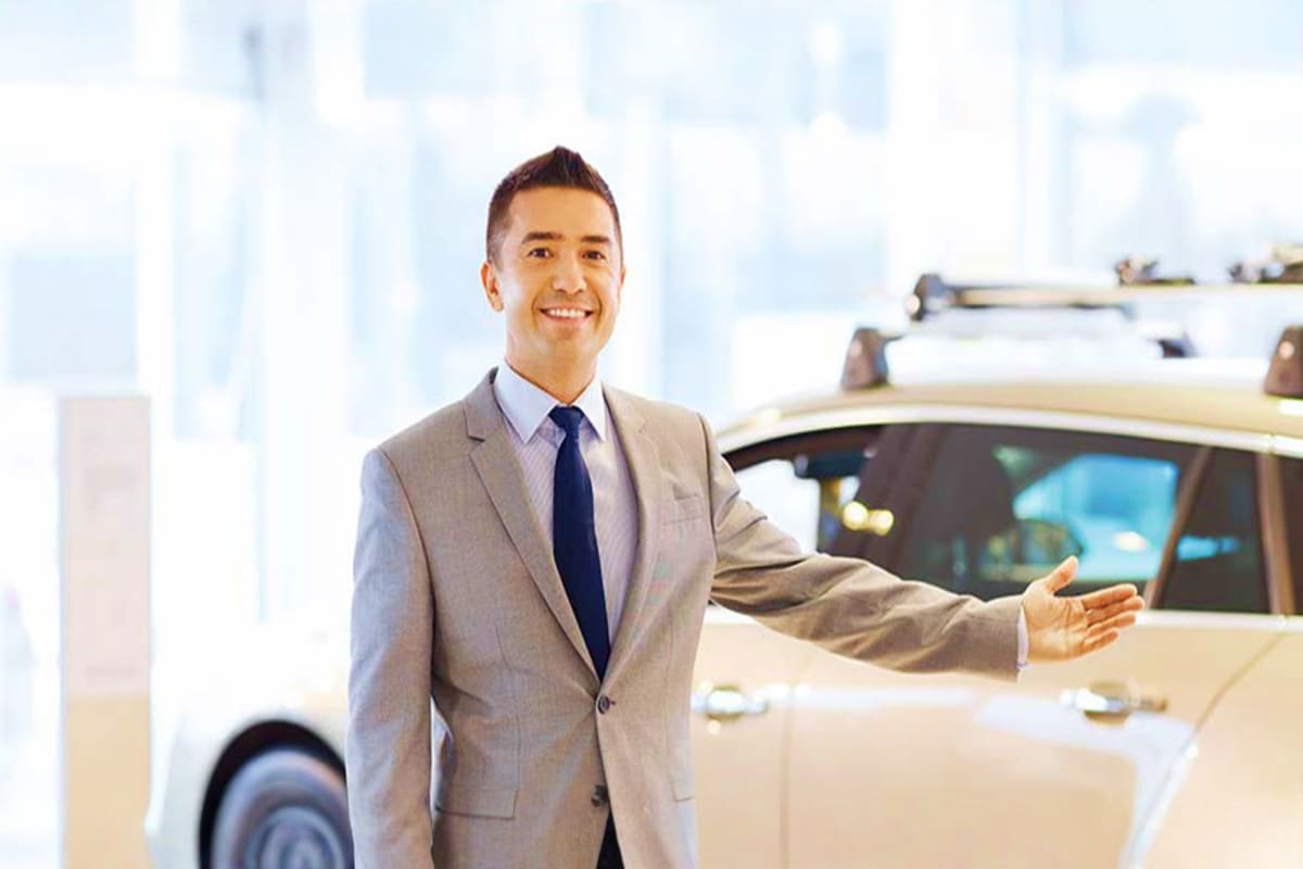 Professional driver in gray suit standing next to white SUV with city skyline in background
