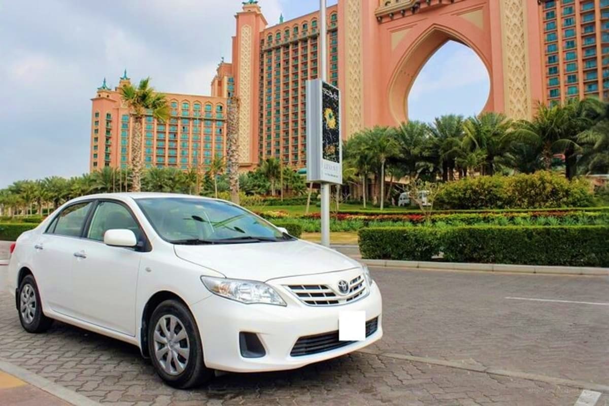 White Toyota sedan parked in front of Atlantis The Palm hotel with distinctive pink archway and palm trees in Dubai