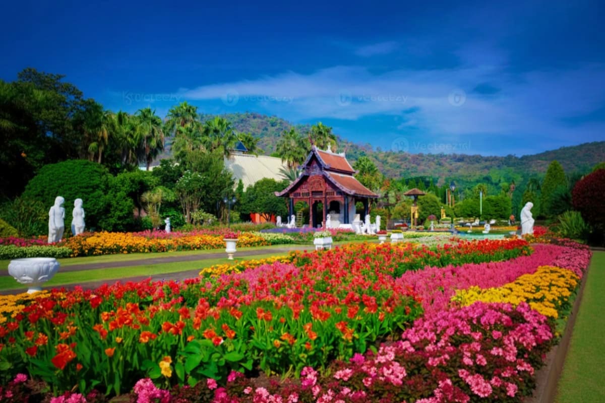 Colorful flower gardens with red tulips and pink flowers in foreground, traditional Thai temple with red roof in background a