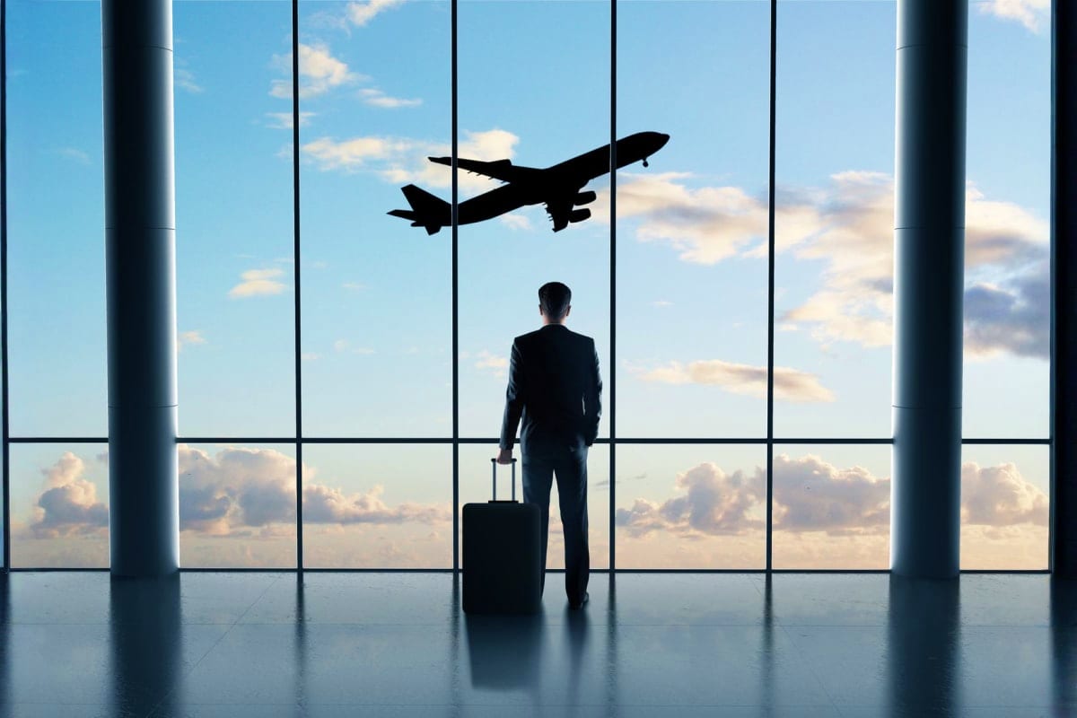 Businessman in silhouette watching airplane taking off through airport terminal window while holding luggage