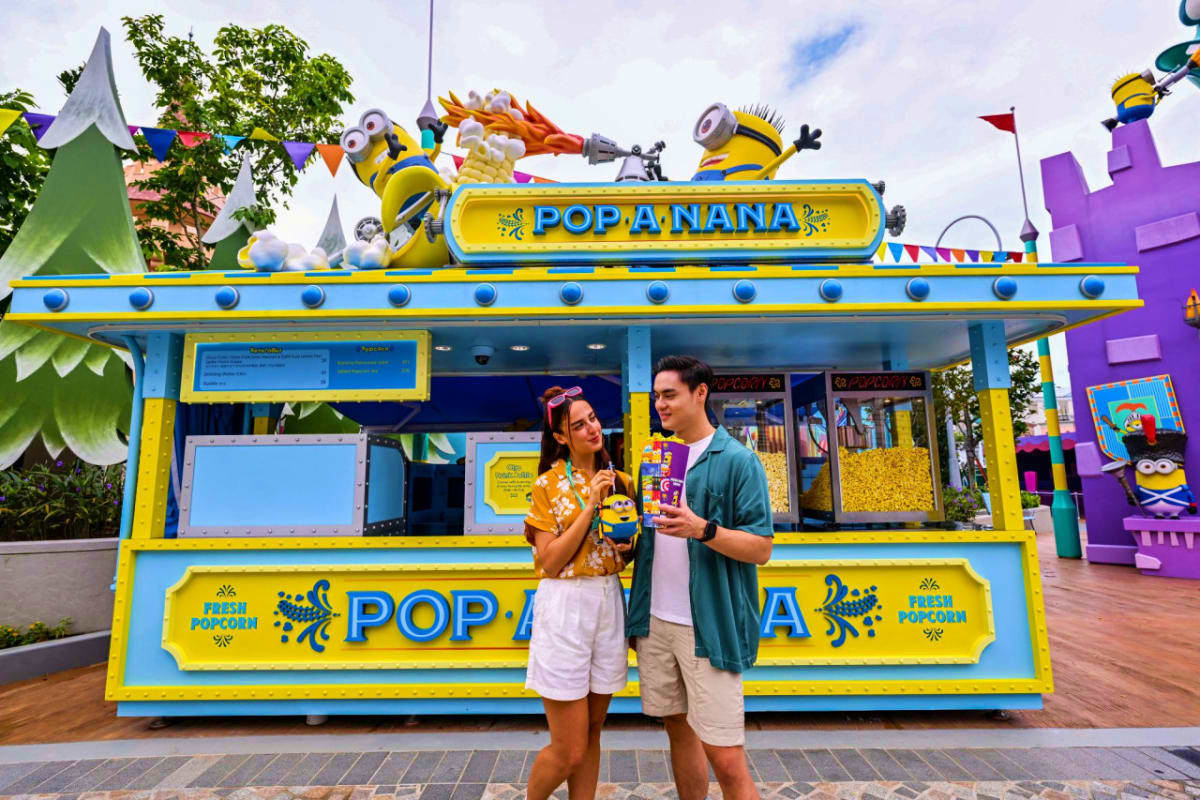 Universal Studios Singapore Two visitors stand outside a colorful Pop a Banana food stand at Universal Studios Singapore, with Minion characters and them