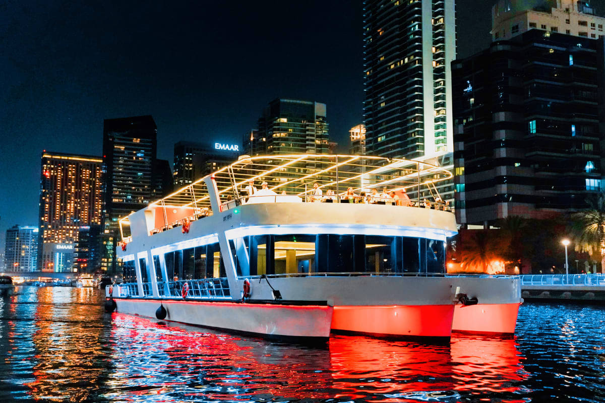 Xclusive Dinner cruise Modern illuminated dinner cruise boat with red and white hull moored on Dubai creek at night, surrounded by lit skyscrapers