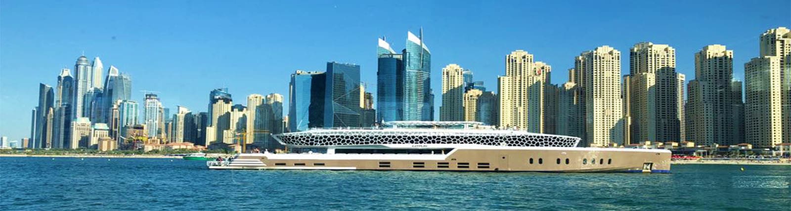 Luxury mega yacht with distinctive perforated roof docked in clear blue waters with Dubai Marina skyscraper skyline in backgr