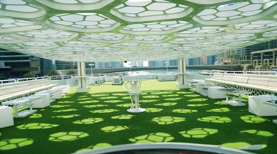 Modern rooftop garden on a mega yacht with green artificial turf, geometric skylight ceiling, white planters, and city skylin