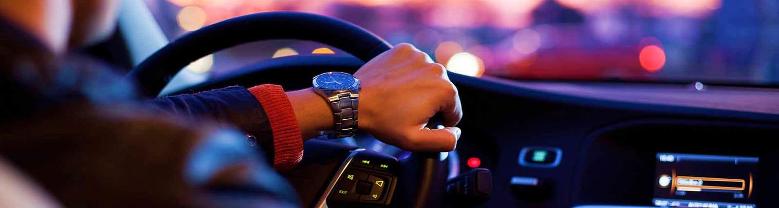 Driver's hand on steering wheel wearing watch while driving car during sunset in Dubai traffic