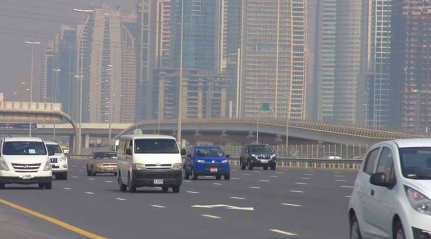 Vehicles driving on Dubai highway with modern skyscrapers and elevated highway overpass in background