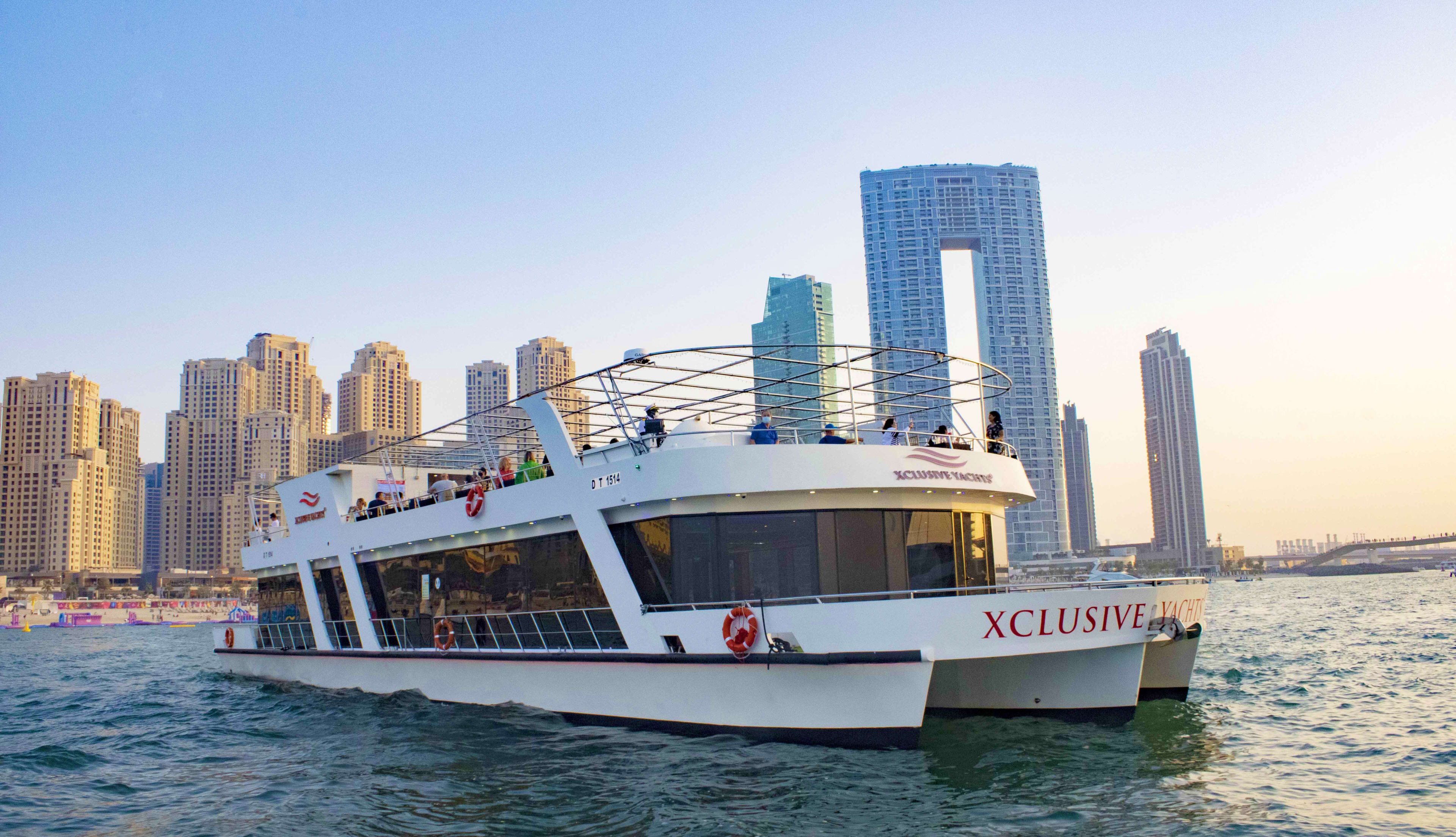 Xclusive Yacht cruise boat on Dubai water with modern skyscrapers and distinctive square tower building in background