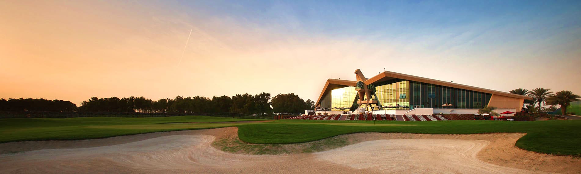 Golf ball on tee with Emirates Golf Club clubhouse building in background on manicured green fairway (2)