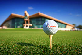 Golf ball on tee with Emirates Golf Club clubhouse building in background on manicured green fairway