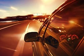 View from inside a car driving on a highway at sunset with headlights on and road stretching ahead