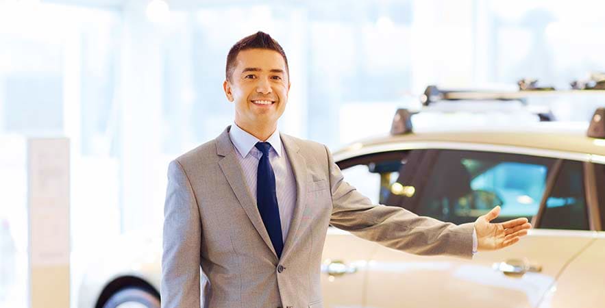 Smiling male chauffeur in business suit standing beside white taxi car at airport terminal