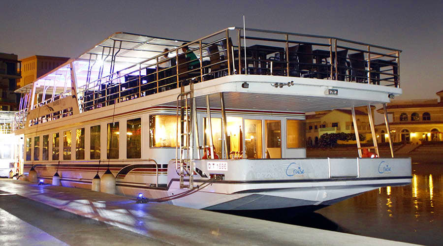 Interior of dinner cruise boat with purple ambient lighting, rows of dining tables, and large windows showing city lights (2)
