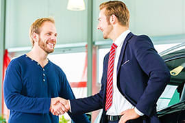 Singapore Cruise Drop off Two men shaking hands at a car dealership or rental service counter with vehicles visible in background