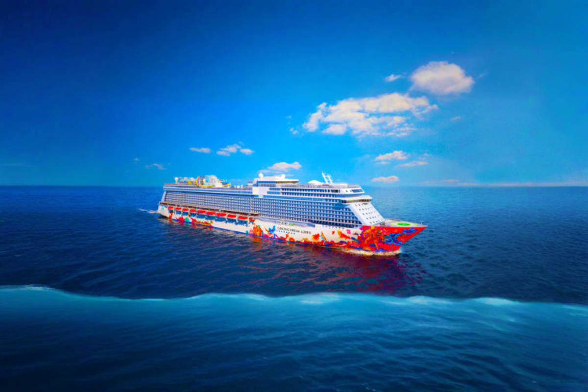 Large modern cruise ship with colorful red hull sailing on blue ocean water under clear sky with white clouds