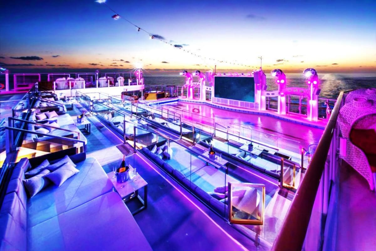 Genting Dream cruise ship deck at sunset with neon pink lighting, lounge seating, and ocean horizon at dusk