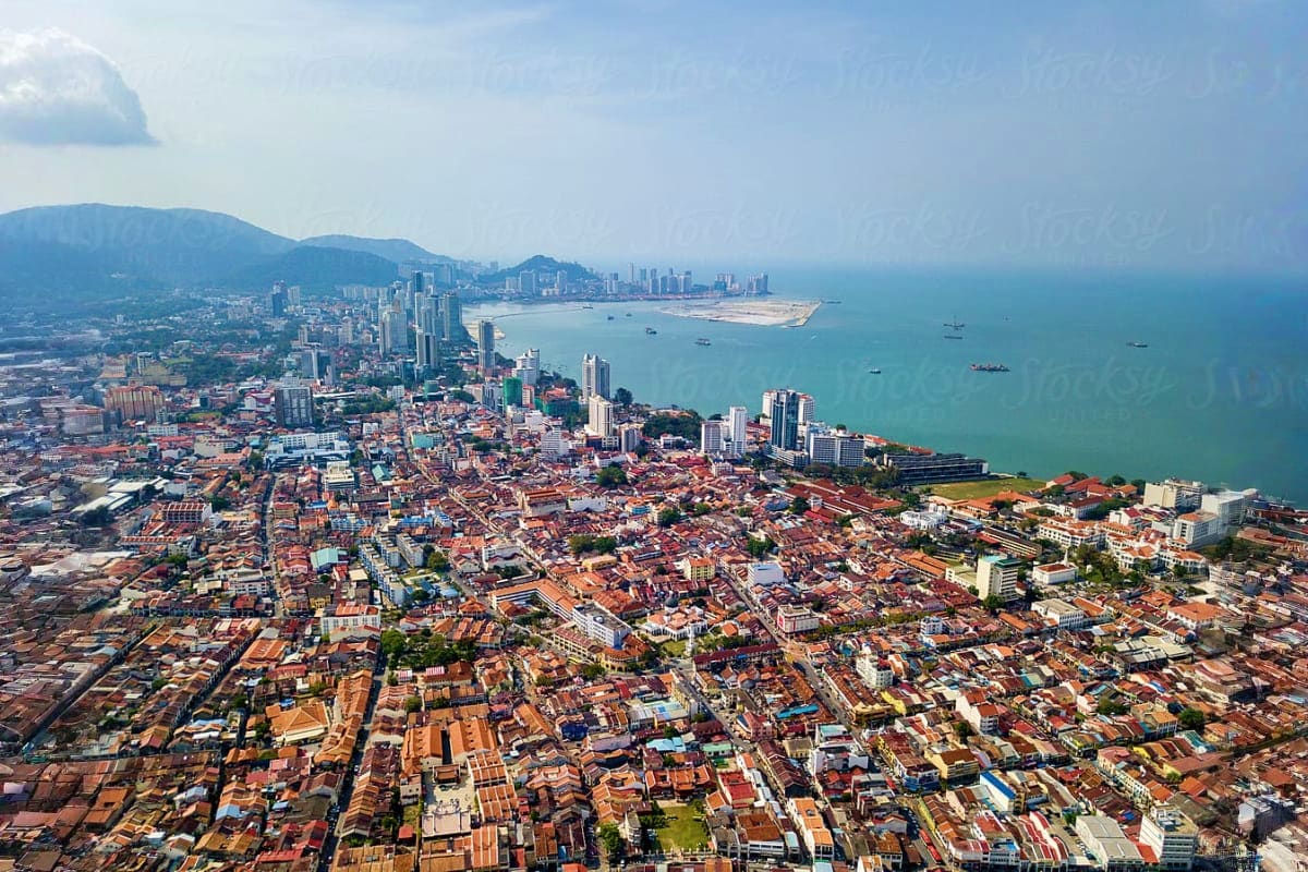 Aerial view of Penang cityscape with turquoise waters, ships, and surrounding mountains during daylight
