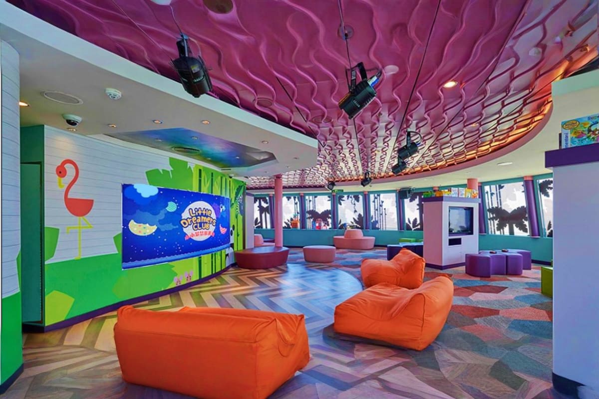 Colorful kids club interior on Genting Dream cruise ship with orange bean bags, purple wavy ceiling, and interactive screen d