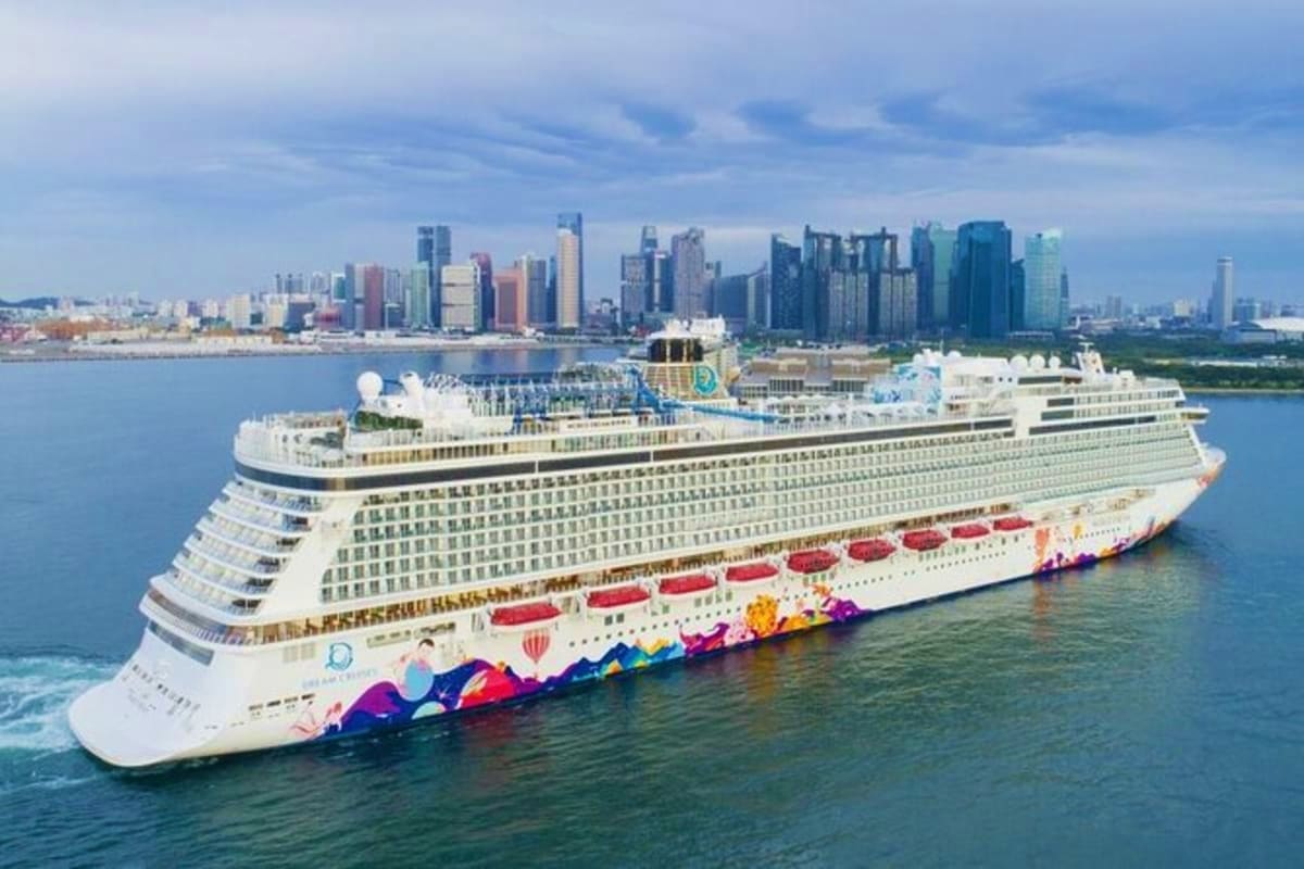 Large white cruise ship with colorful hull art sailing in blue waters with city skyline in background