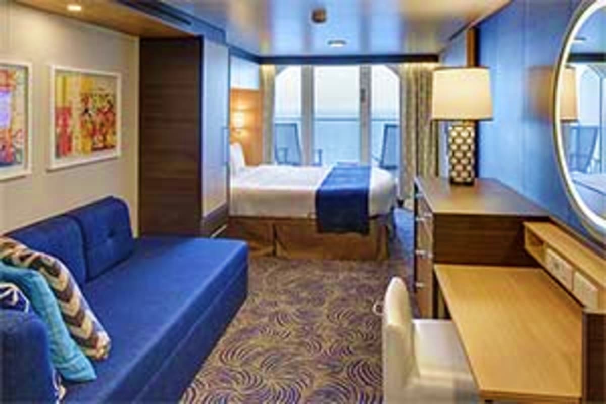 Luxurious cruise ship stateroom with queen bed, blue sofa, ocean view windows, and modern furnishings