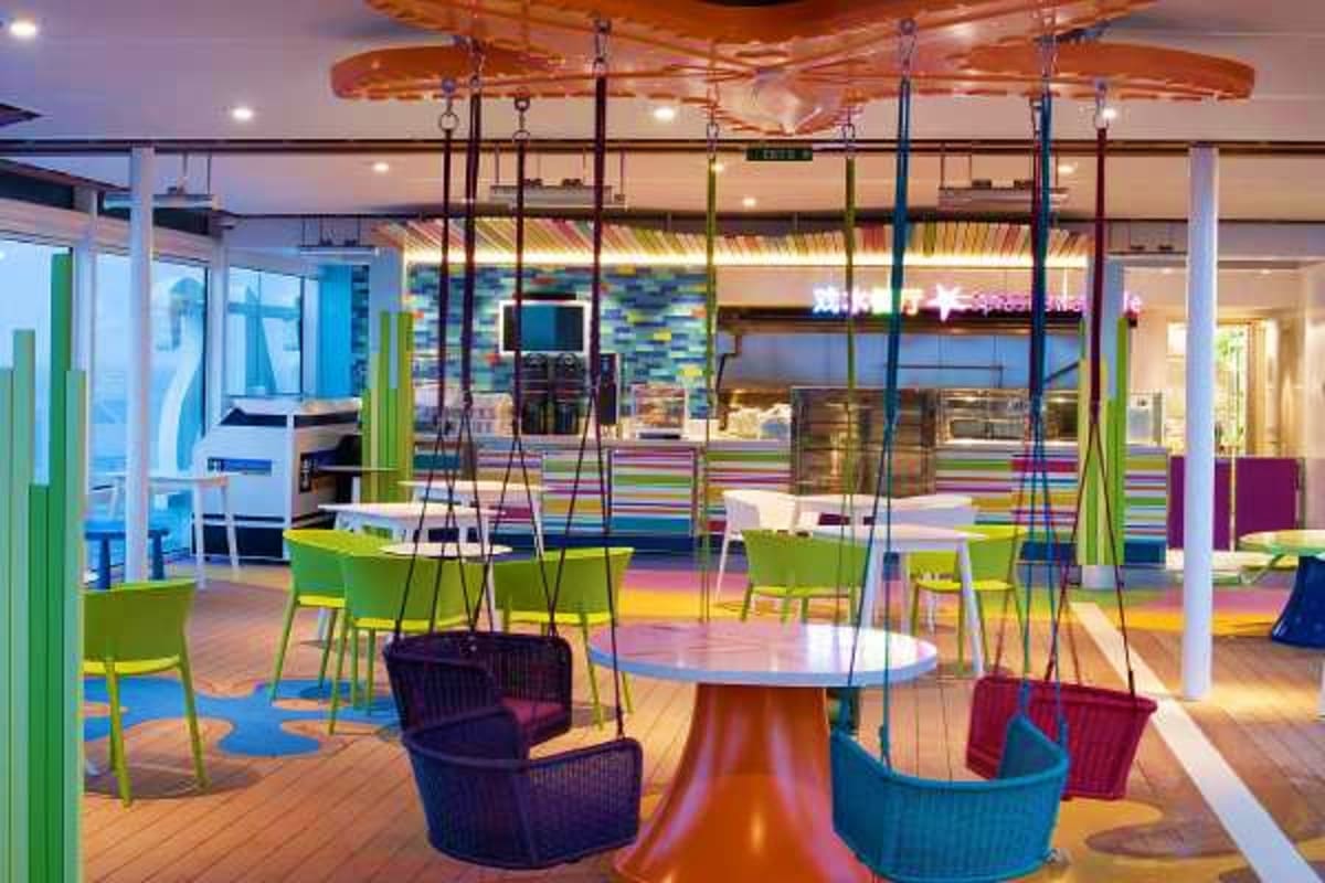 Modern cruise ship interior with colorful suspended swing seating, green chairs, and vibrant floor patterns in open lounge ar