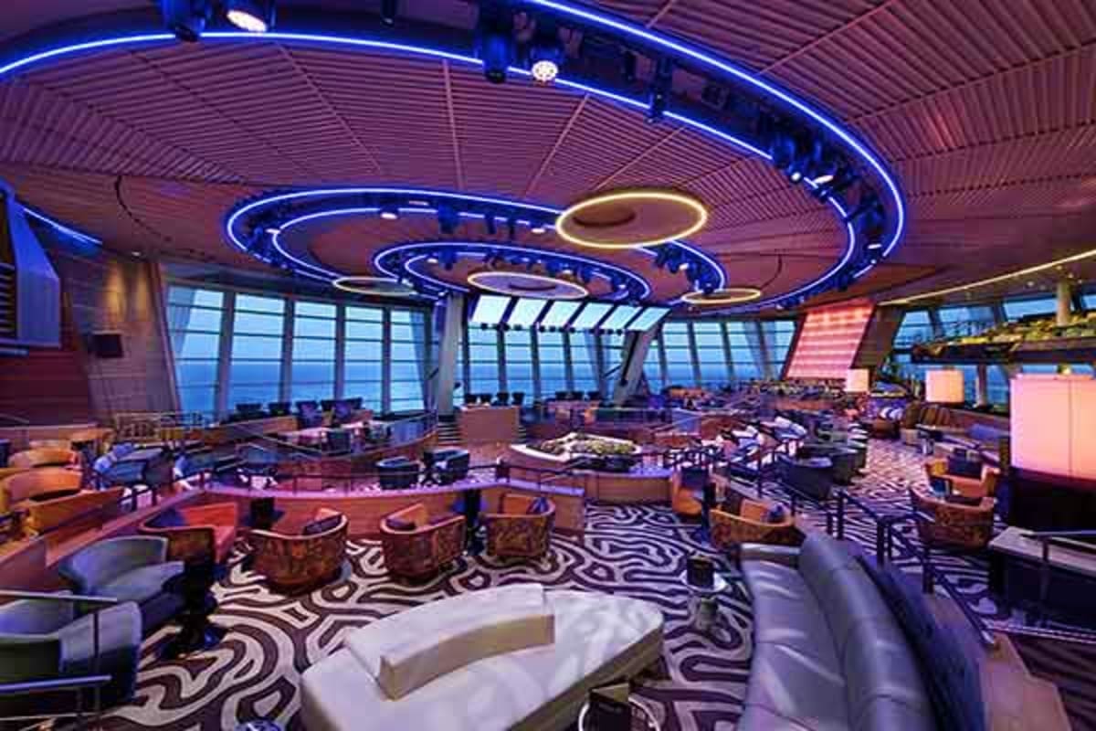 Modern cruise ship nightclub with blue neon circular lighting, zebra-patterned floor, lounge seating, and floor-to-ceiling wi