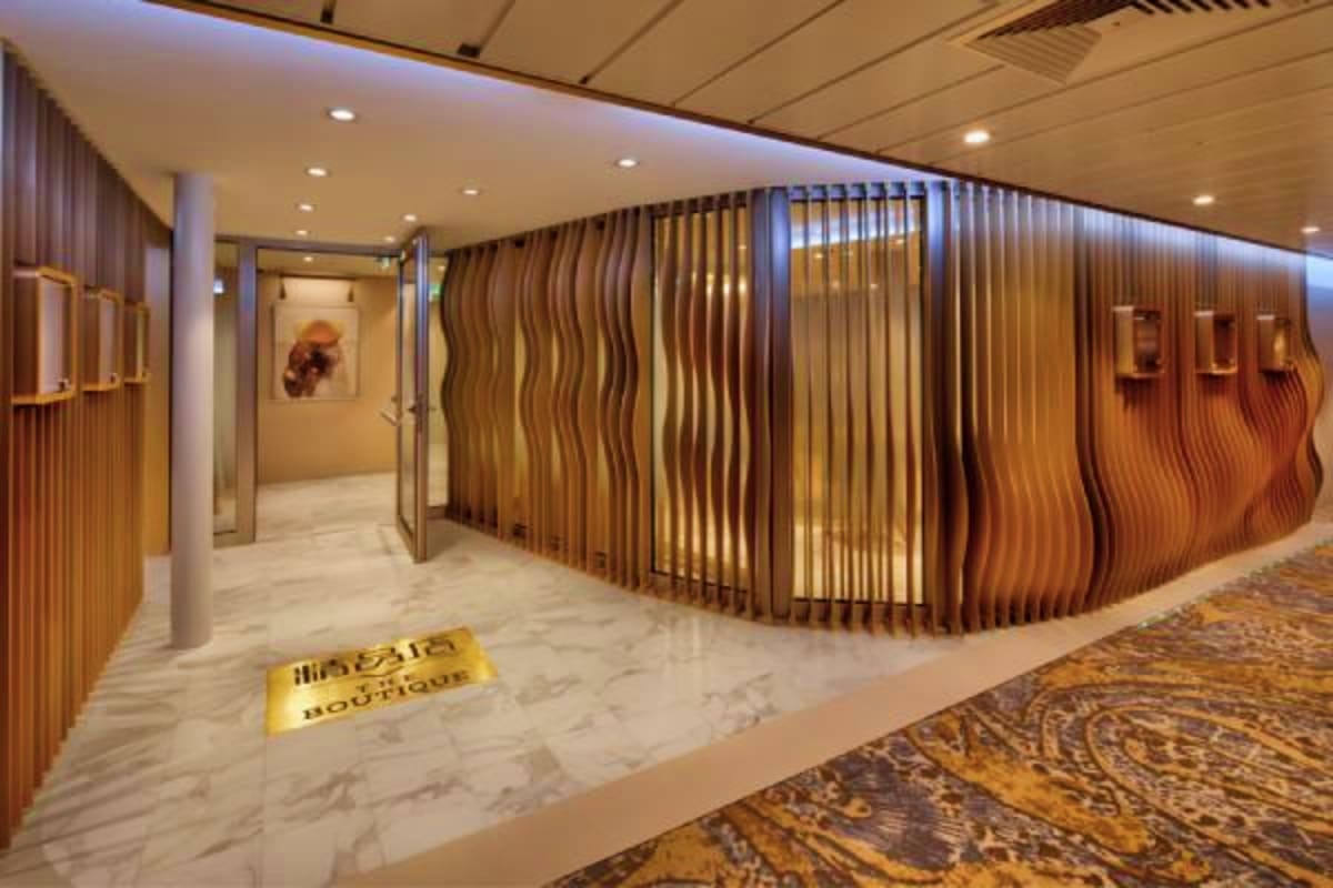 Modern boutique spa entrance with wavy wooden wall panels, marble flooring, and welcoming gold signage in an upscale cruise s