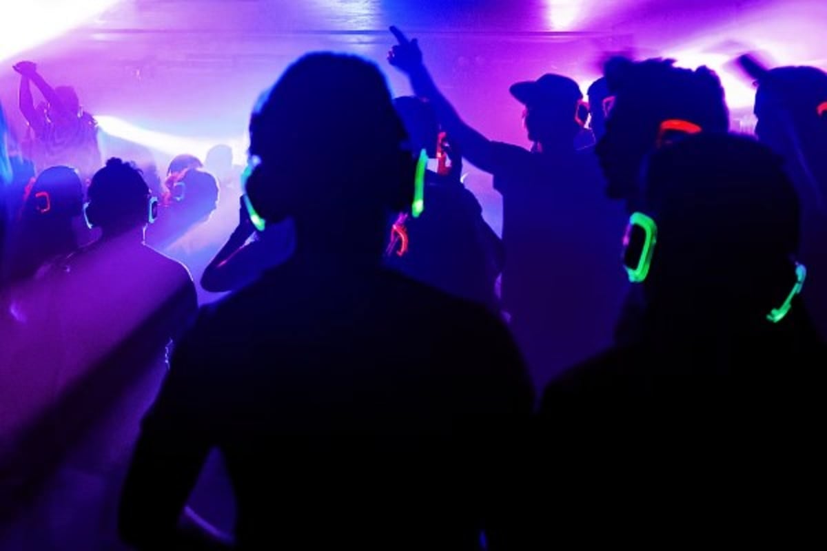 Silhouetted crowd of passengers dancing and enjoying nightlife entertainment with neon glow sticks and purple stage lighting 