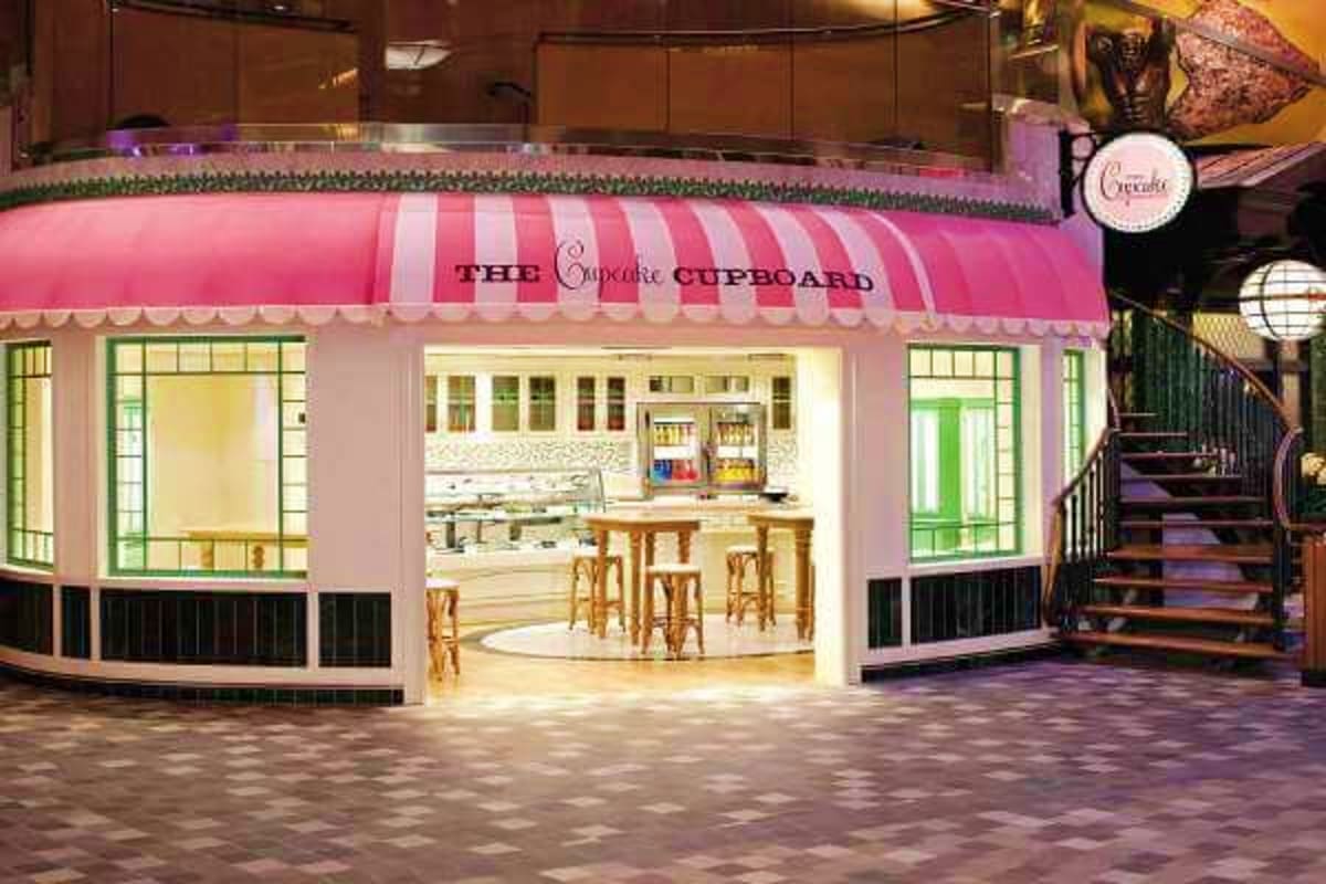 The Cupcake Cupboard bakery storefront with pink and white striped awning and large windows displaying counter seating inside