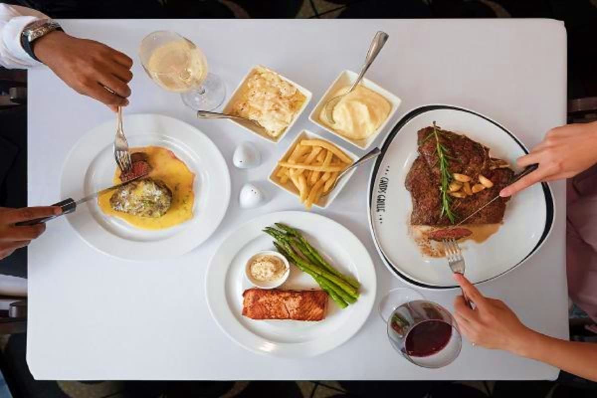 Overhead view of fine dining meal with steak, salmon, sides, and wine glasses on white plates and table